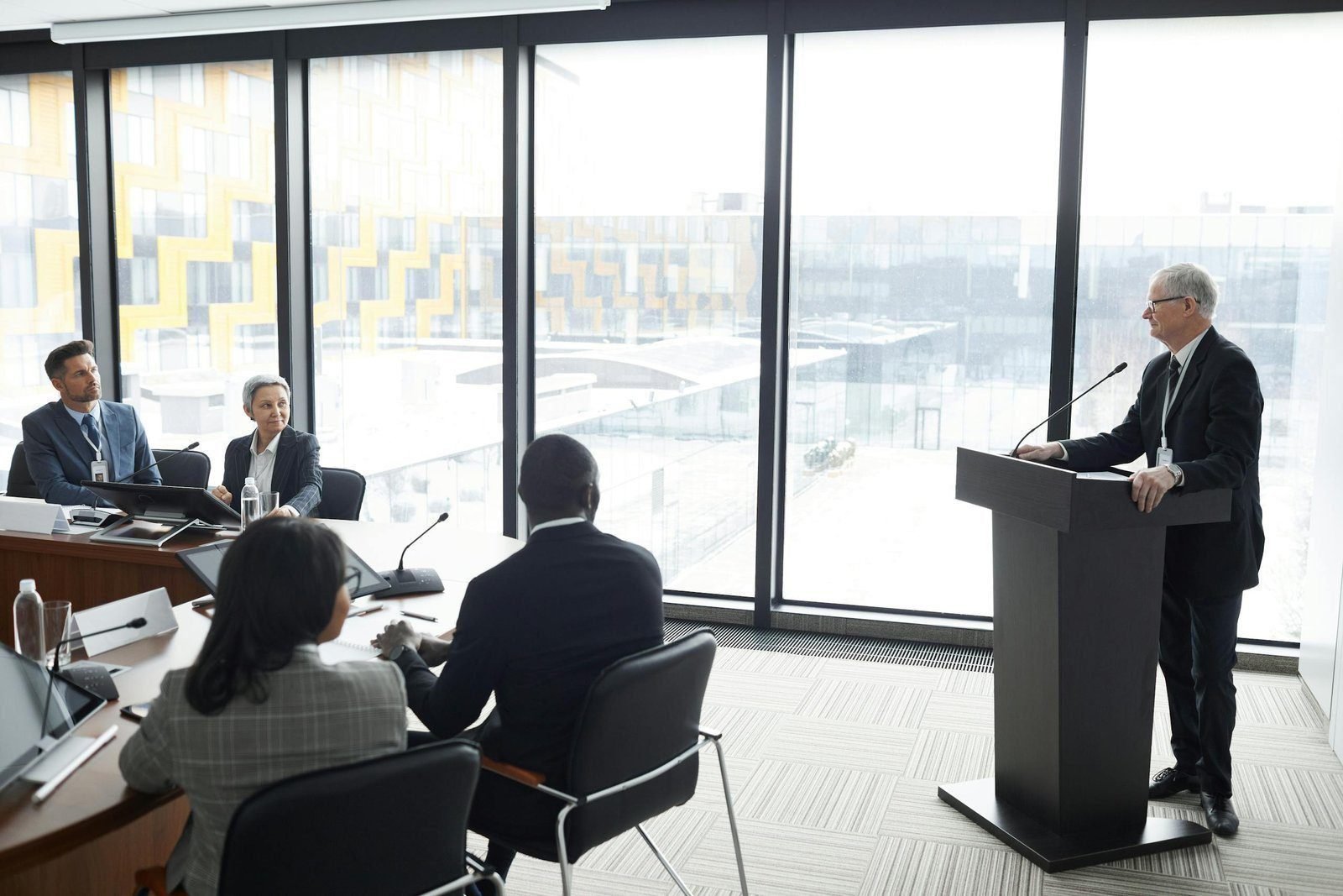 Everyone Wants To Be Wanted 1 Corporate professionals engaged in a formal business meeting in a modern conference room setting.