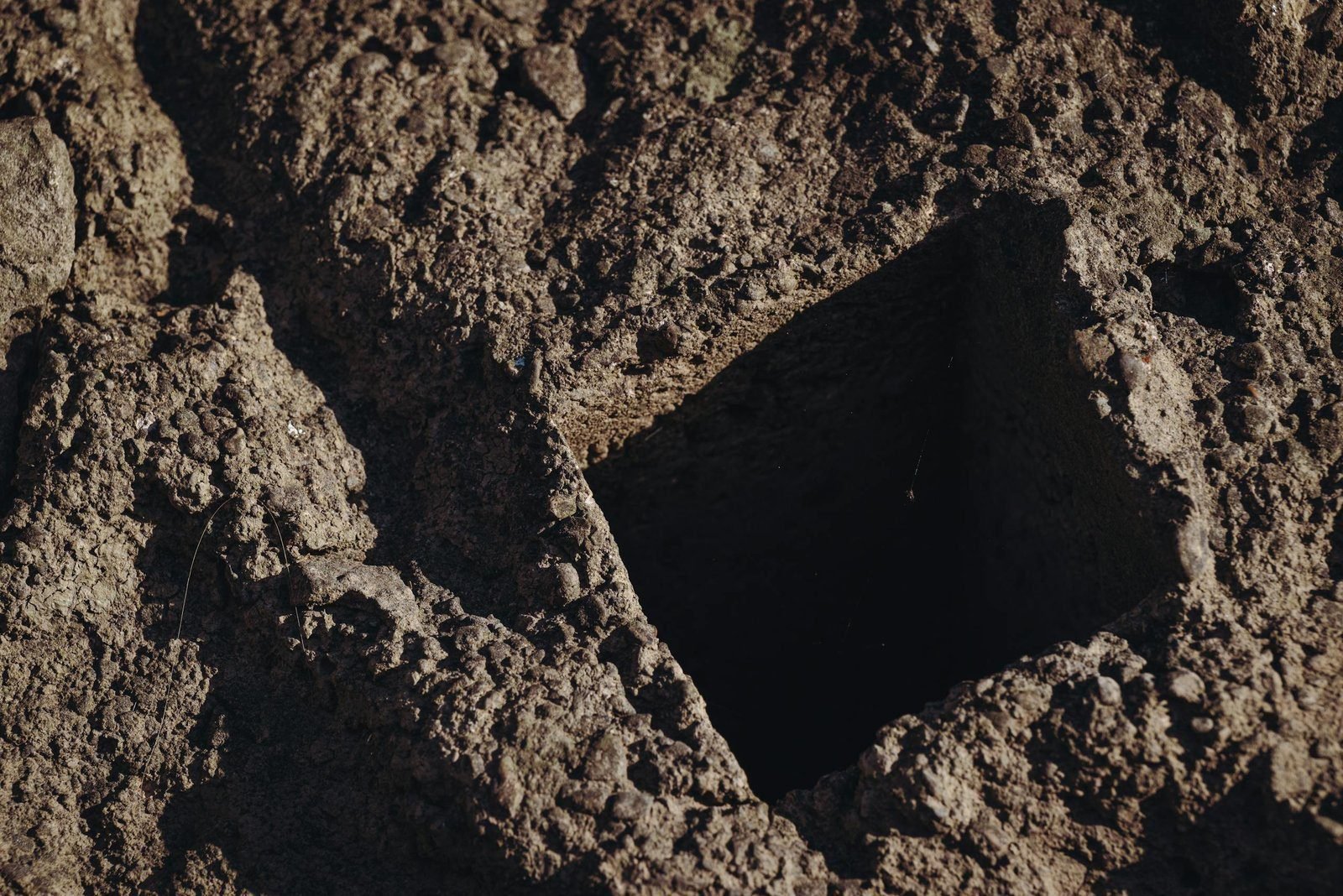 If You’re in a Hole, Stop Digging 1 Close-up view of a rectangular hole dug into a rough, textured soil surface, showcasing geological features.